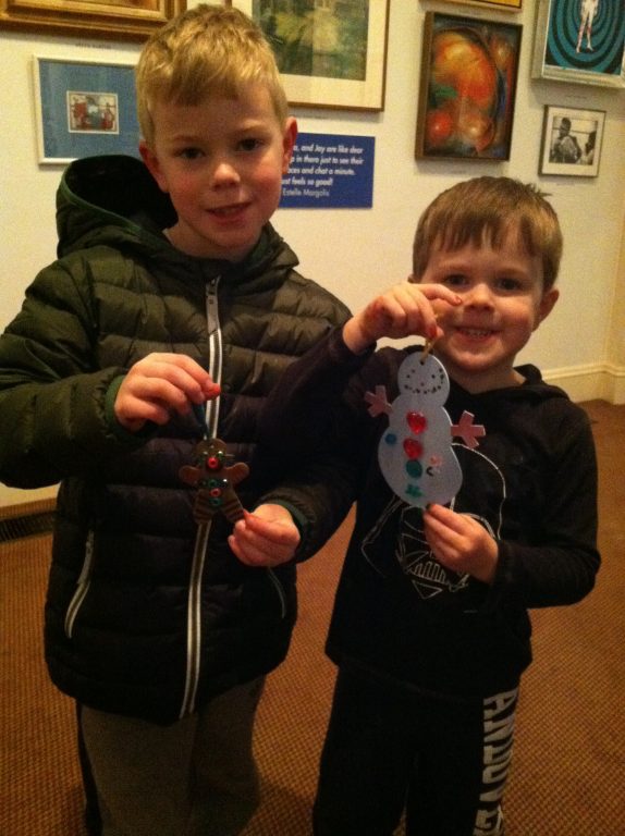 Two boys smiling and holding up hand made holiday ornaments