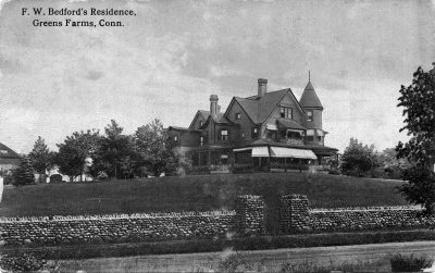 Black and white photograph of a Victorian mansion with a grassy lawn, stone wall and gate.